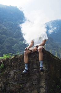 A person sitting on a cliff and vaping