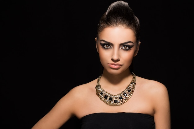 photo vogue. beautiful woman posing in black dress waring Necklaces.